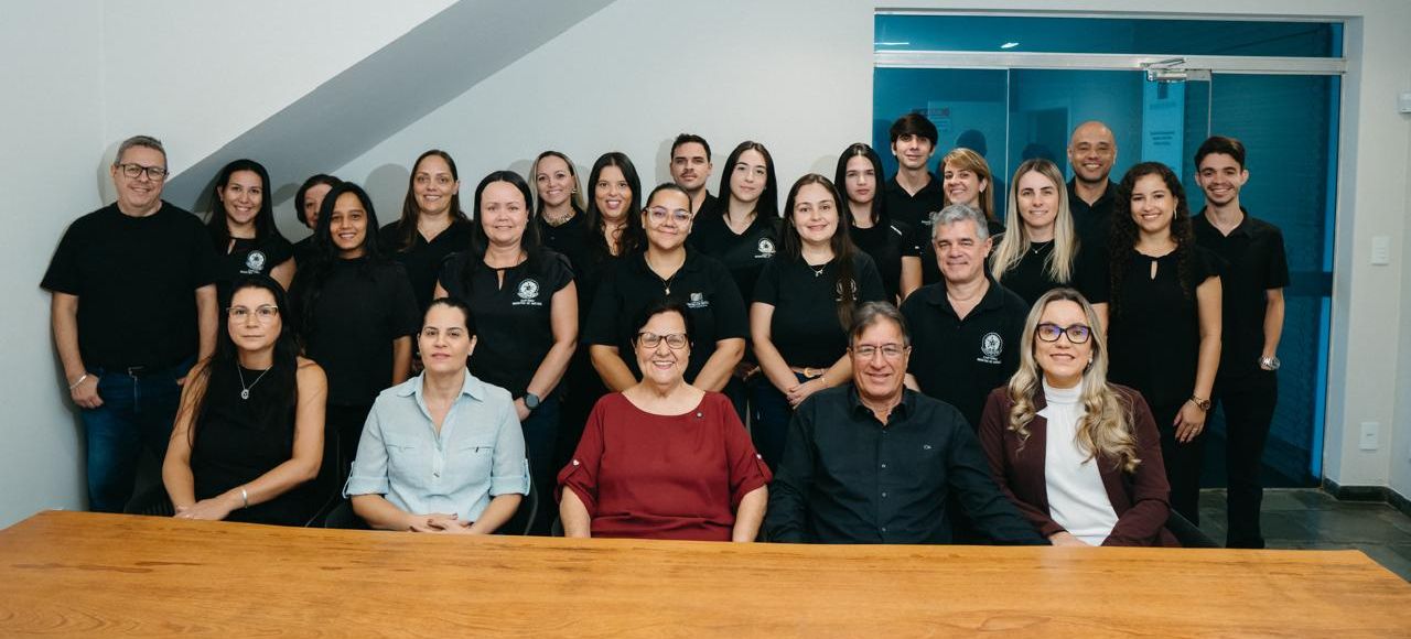 Equipe do cartório reunida atrás da mesa de atendimento: cerca de vinte e cinco pessoas, a maioria de camiseta preta com o símbolo do registro